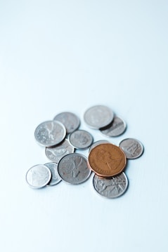 A collection of assorted coins with one larger brown coin placed prominently on top of several smaller silver coins on a light blue surface.
