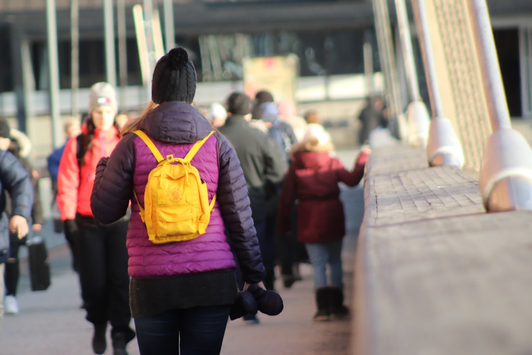 woman in purple jacket and yellow backpack walking on sidewalk during daytime
