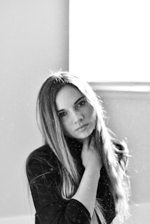 A black and white portrait of a person with long hair looking into the camera. The lighting is soft and dust particles are visible in the air, creating a dreamy effect.