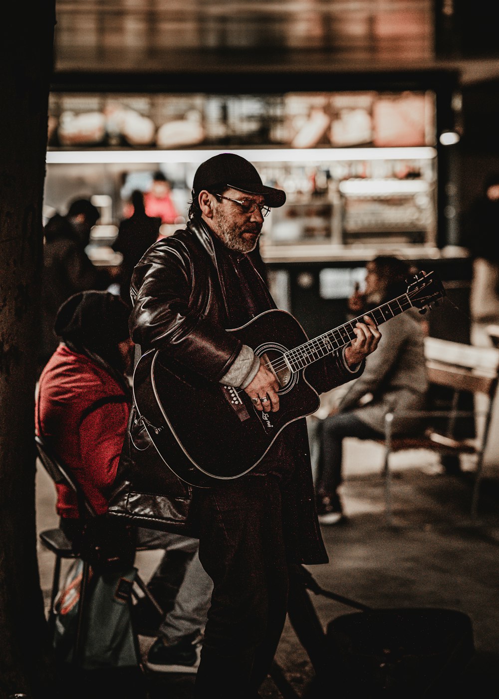 hombre con chaqueta negra tocando la guitarra acústica