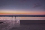 Serene infinity pool at a Karjat villa surrounded by lush greenery under a twilight sky.