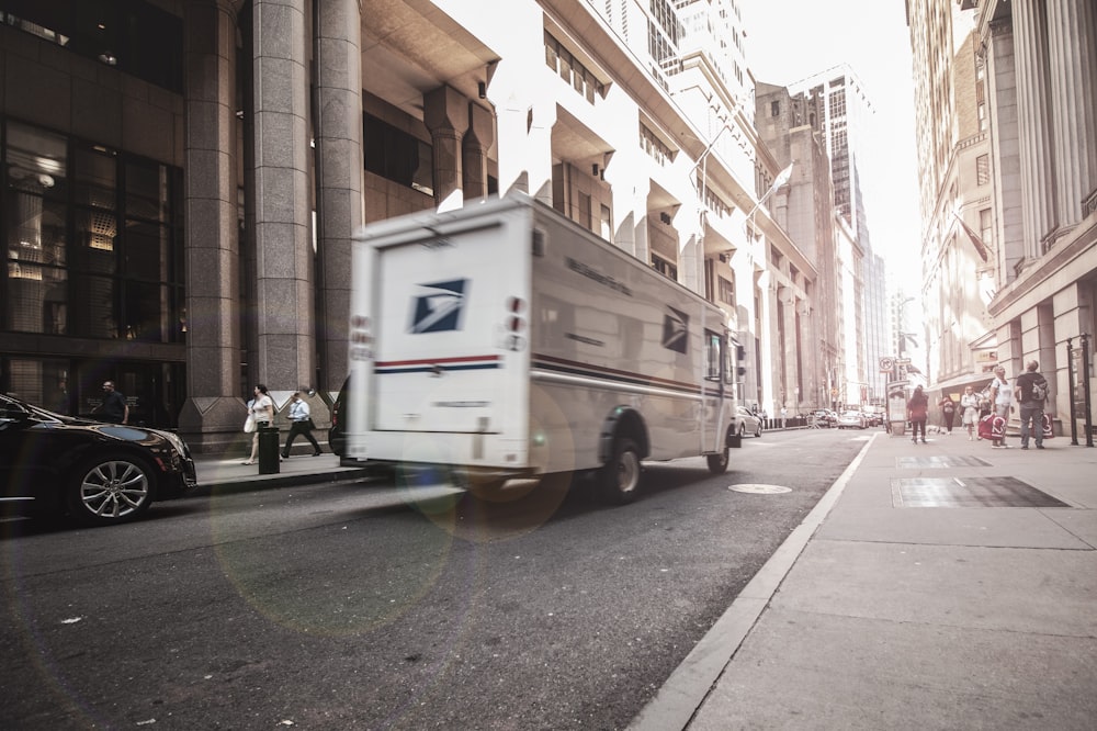 昼間、茶色のコンクリートの建物の脇に停車する白いバン
