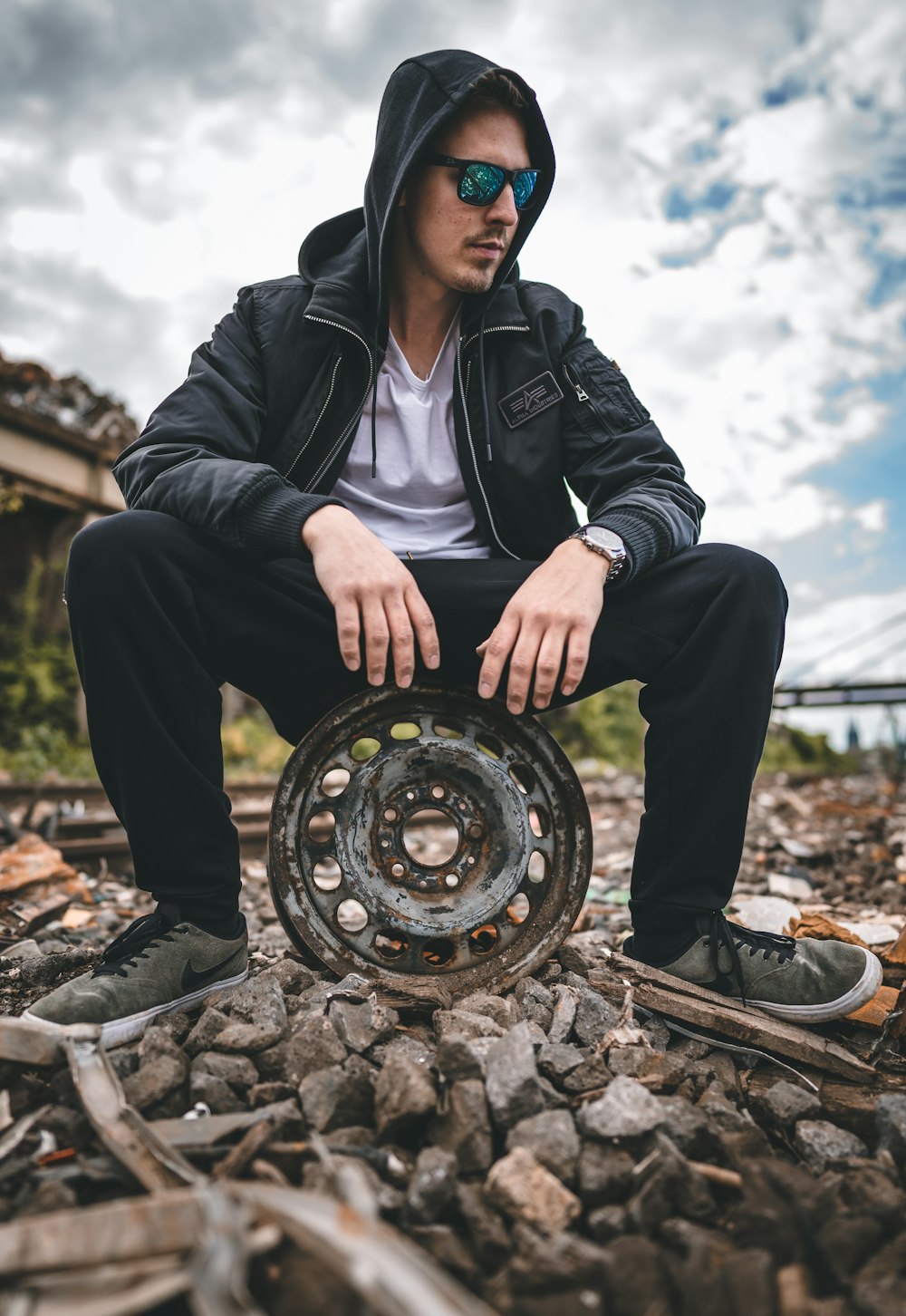 man in black leather jacket and black pants sitting on brown metal wheel during daytime