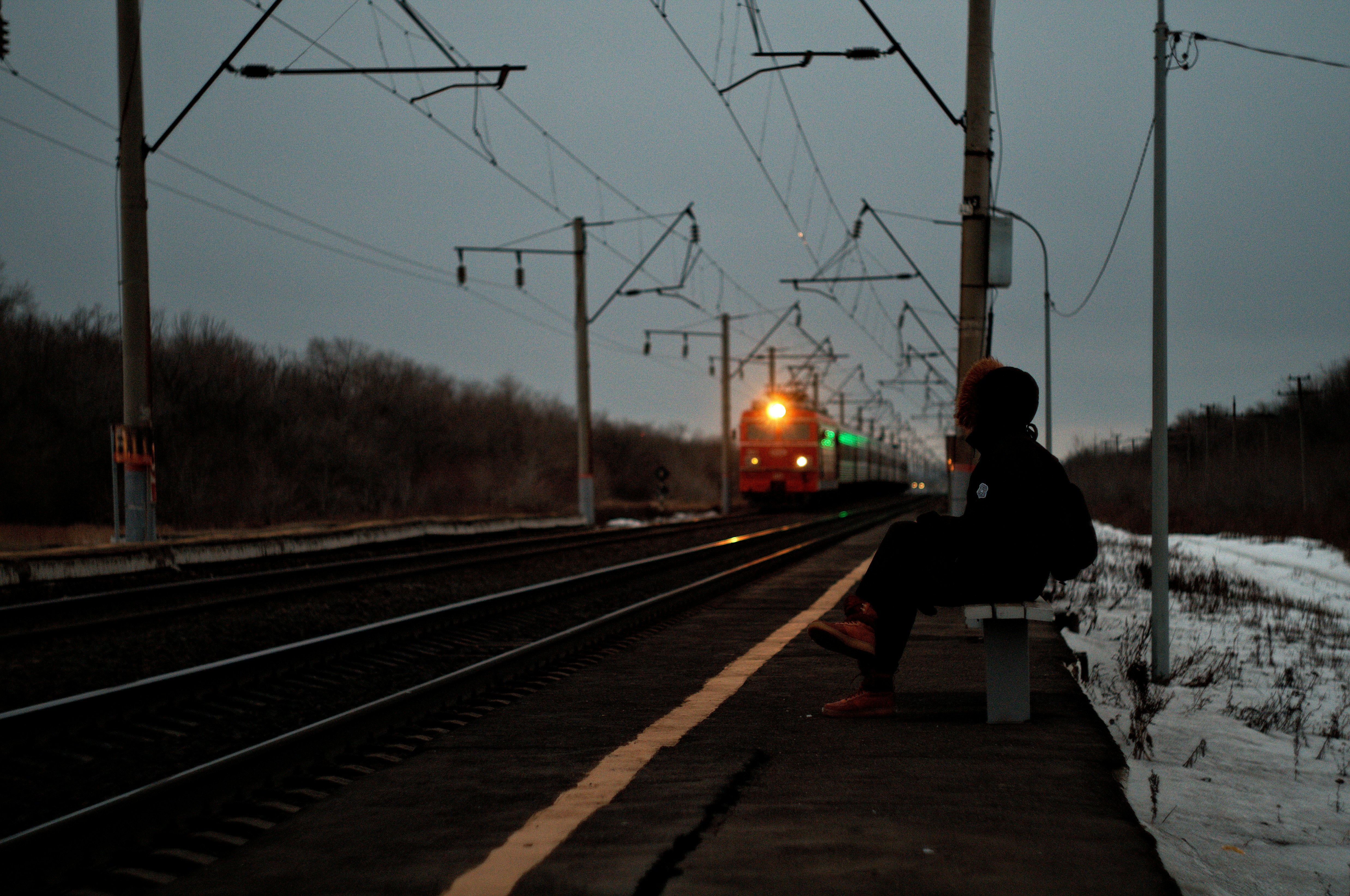 Man In Black Jacket Sitting On Bench Near Train Rail During Night
