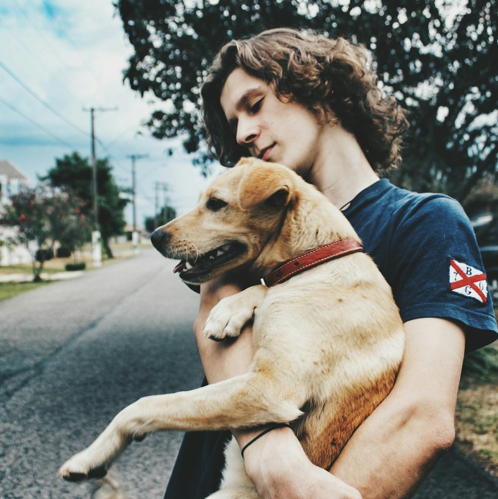 man in black t-shirt hugging brown short coated dog