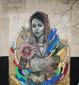 A mural features a woman wearing a headscarf with a serene expression. She holds colorful flowers, and there are vibrant, abstract shapes surrounding her. The text 'Your Brand Your Choice' is written on her clothing. The artwork combines realistic portraiture with abstract elements, creating a striking visual contrast.