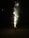 A cone-shaped firework emits colorful sparks and smoke against a dark background. Bright flashes of red, green, and white lights are visible, highlighting the explosive activity.