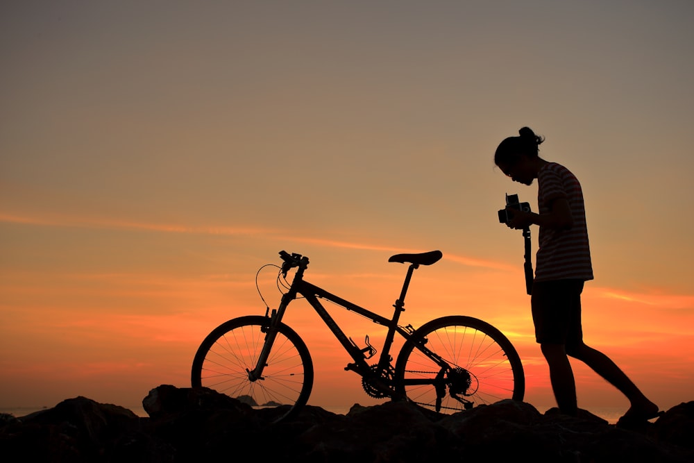 silhouette of man standing beside black mountain bike during sunset