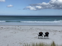 2 people sitting on camping chairs on beach during daytime