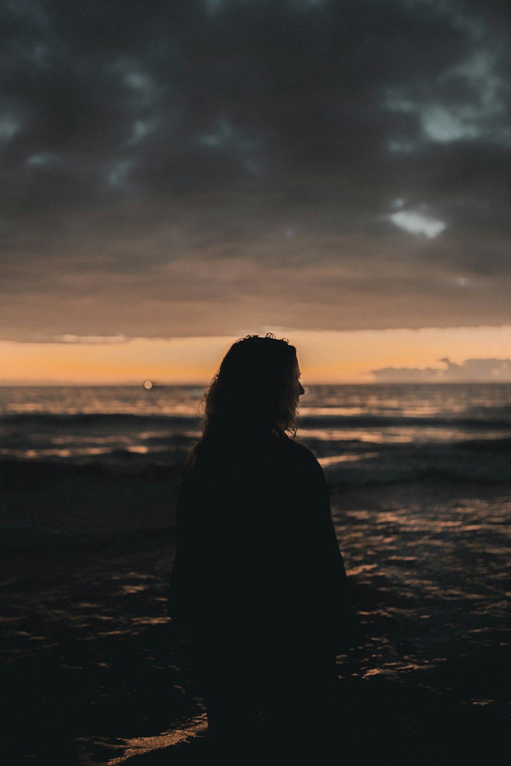 silhouette of woman standing on seashore during sunset