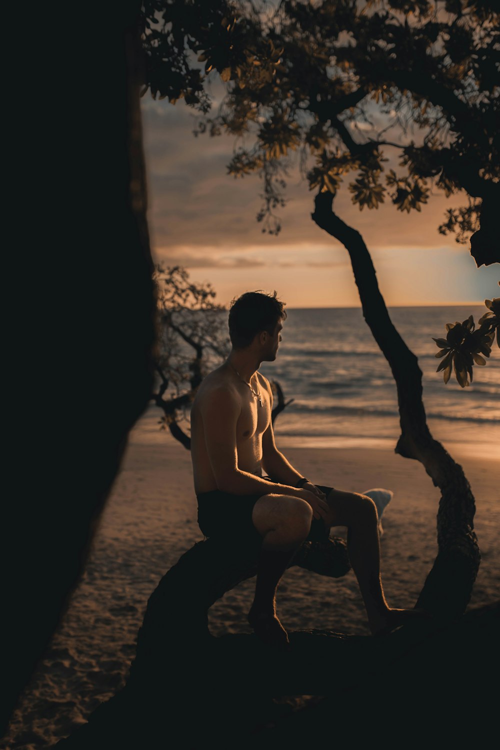 homem de shorts pretos sentado na praia durante o pôr do sol