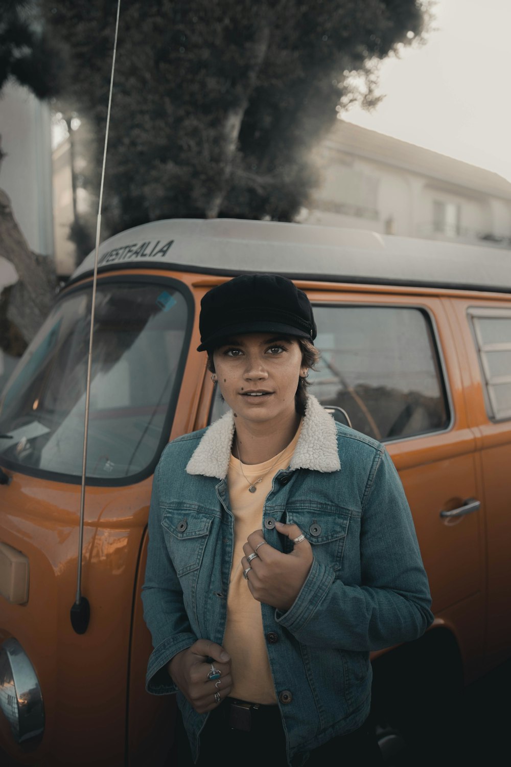 man in blue denim jacket standing beside orange car