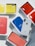 Several iPhone leather folio cases in various colors including yellow, red, blue, and pink are arranged in their packaging. A white iPhone is placed among them, catching the light.