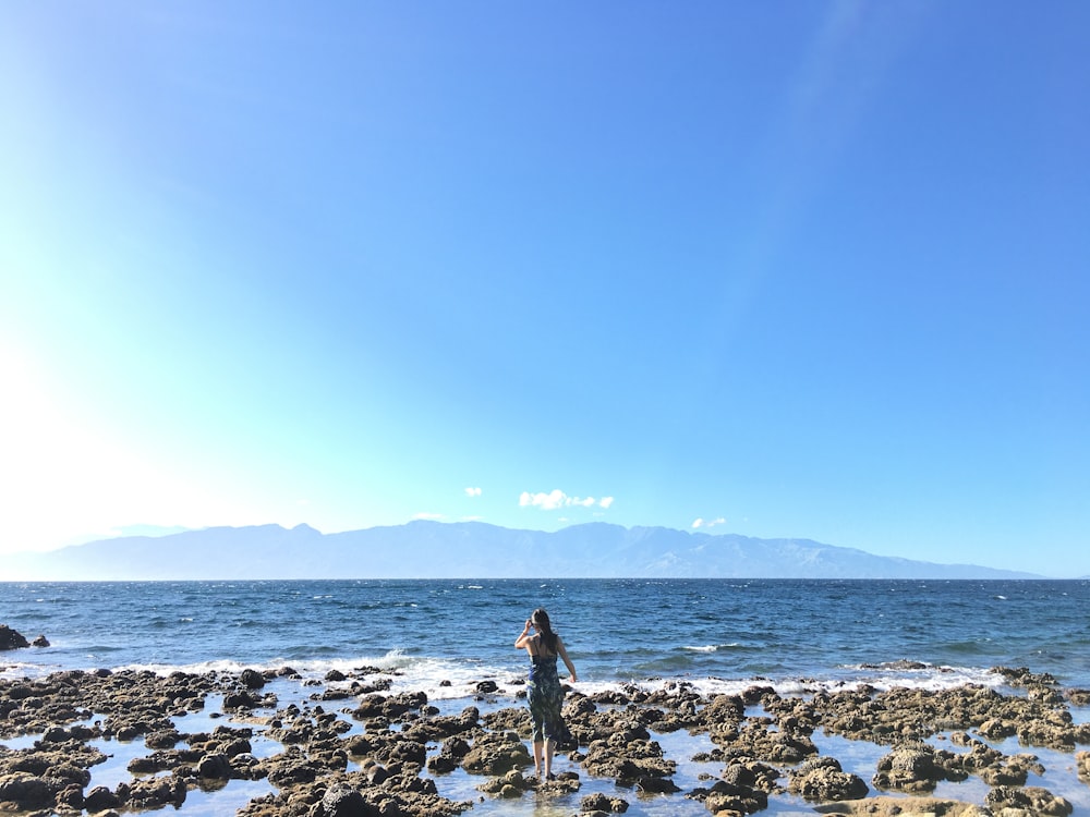 woman in black dress standing on rocky shore during daytime