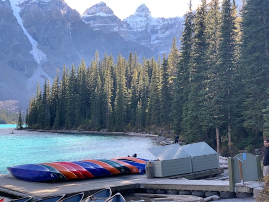 red and white boat on dock near green trees and mountain during daytime in Moraine Lake Canada