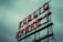 Red neon letters form the words 'PUBLIC MARKET' on a metal framework against an overcast sky.