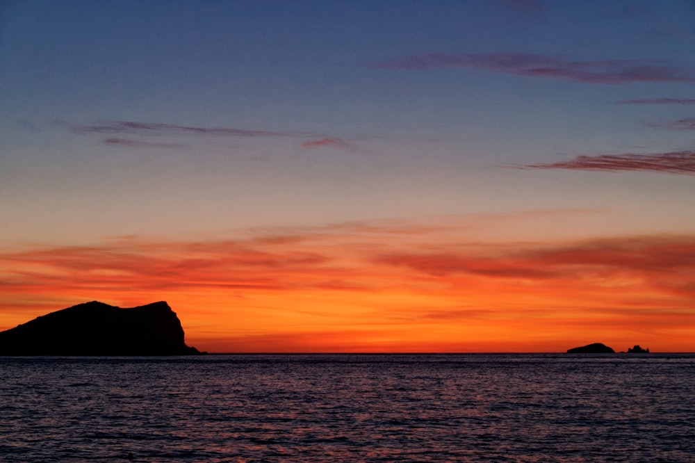 silhouette of mountain beside sea during sunset