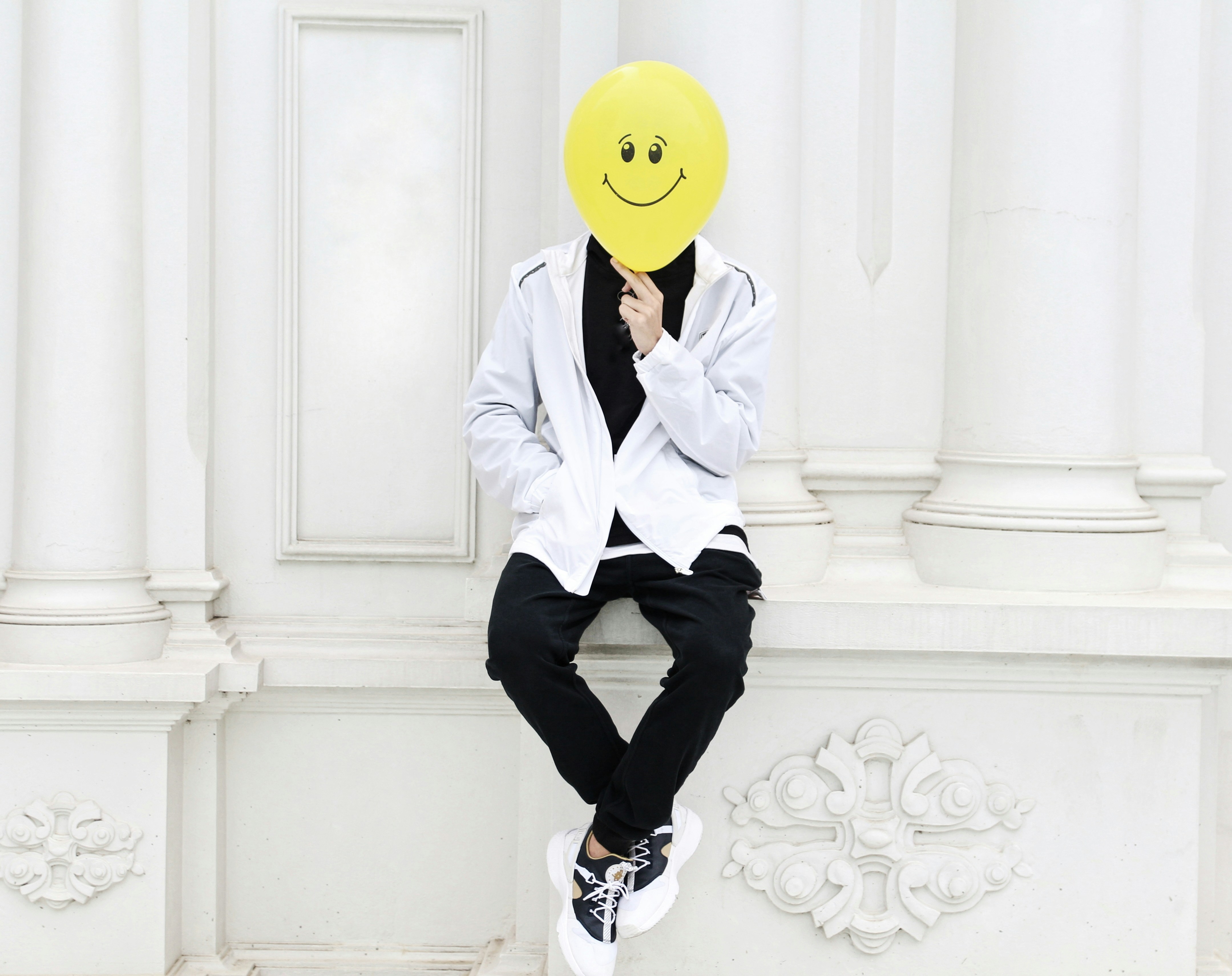 a person with a smiley face mask sitting on a wall
