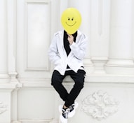 a person with a smiley face mask sitting on a wall
