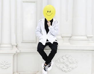 a person with a smiley face mask sitting on a wall