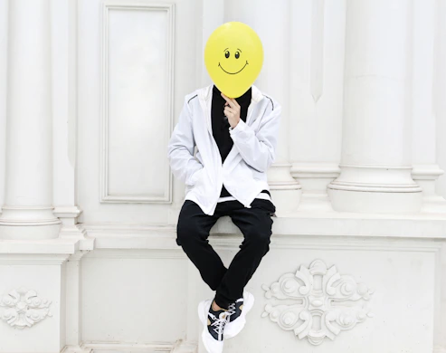a person with a smiley face mask sitting on a wall