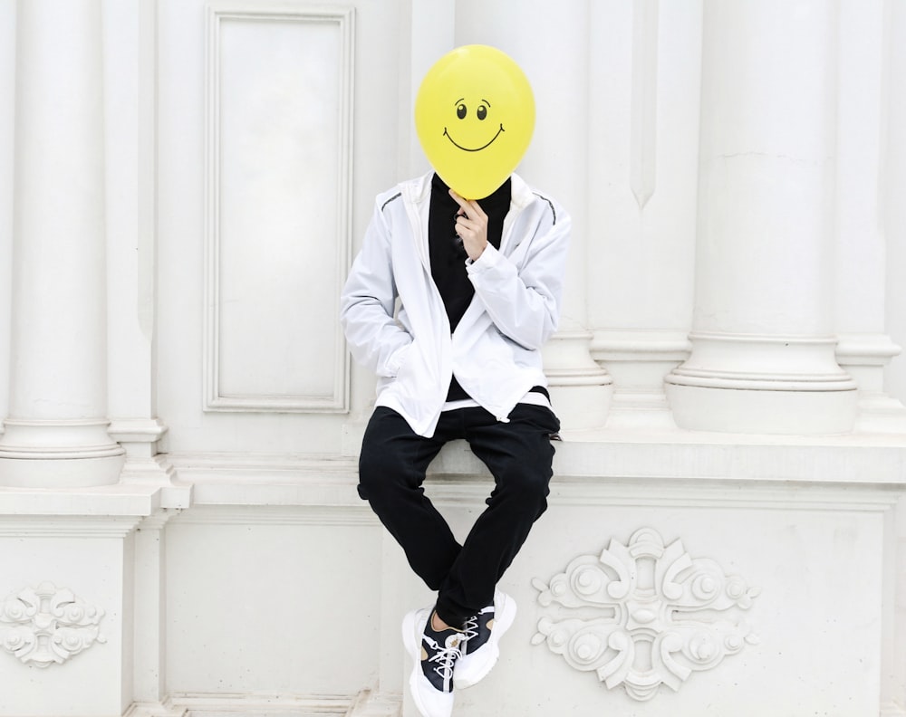 a person with a smiley face mask sitting on a wall