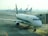 A row of airplanes is parked at an airport gate area, with a focus on the Alitalia aircraft situated closest to the camera. The airplane is connected to a passenger boarding bridge. Several other airplanes are visible in the background, lined up along the tarmac under the overcast sky.
