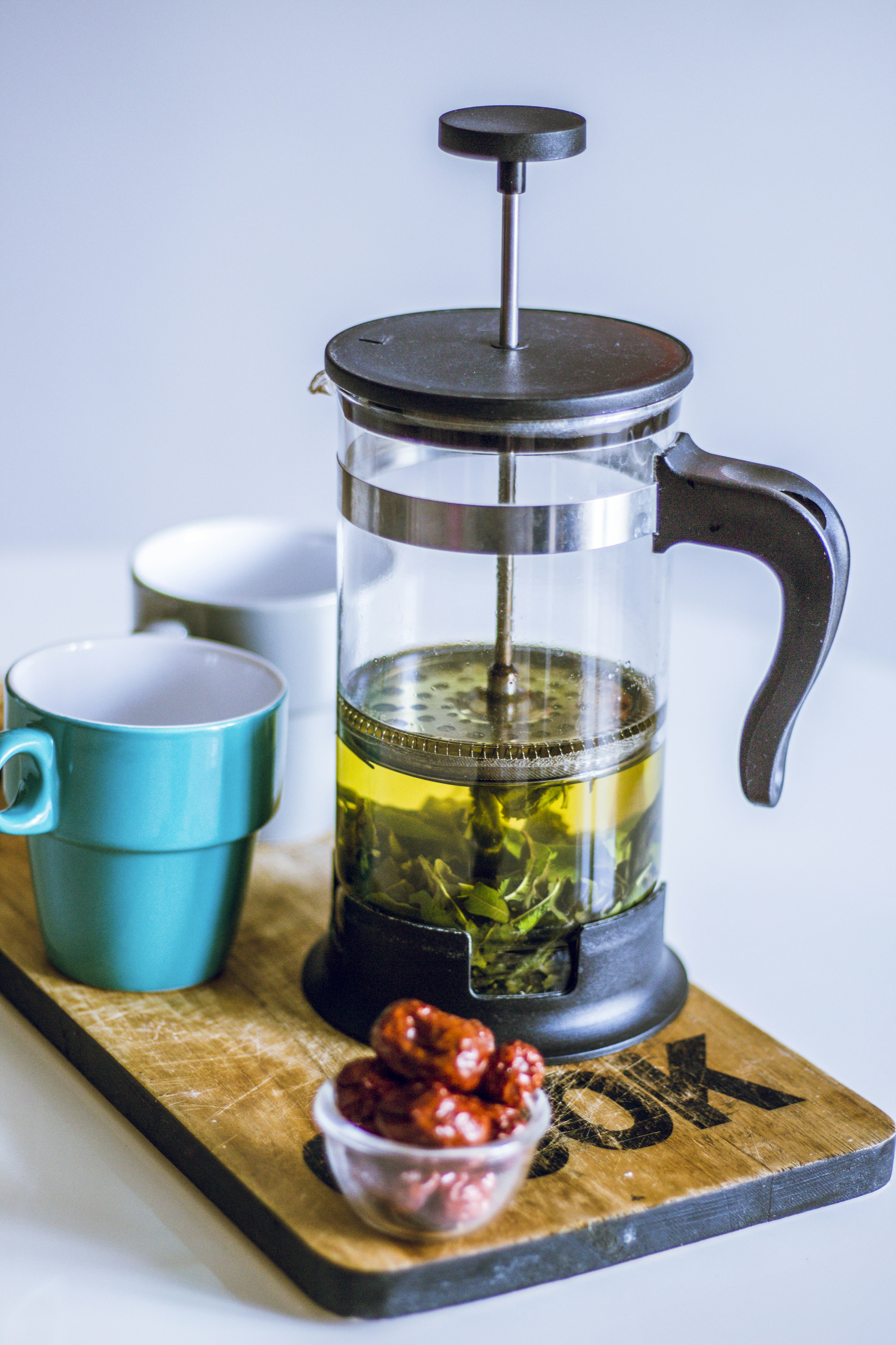 silver and black coffee press beside blue ceramic mug on brown wooden chopping board