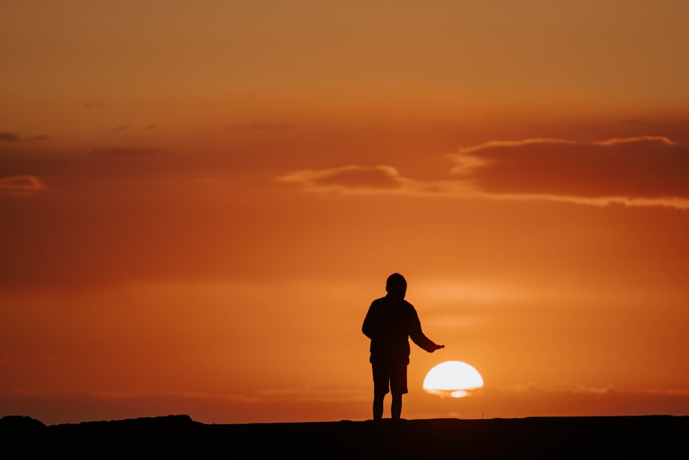 silhouette of man standing on hill during sunset