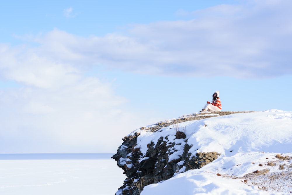 woman in pink jacket sitting on snow covered ground during daytime