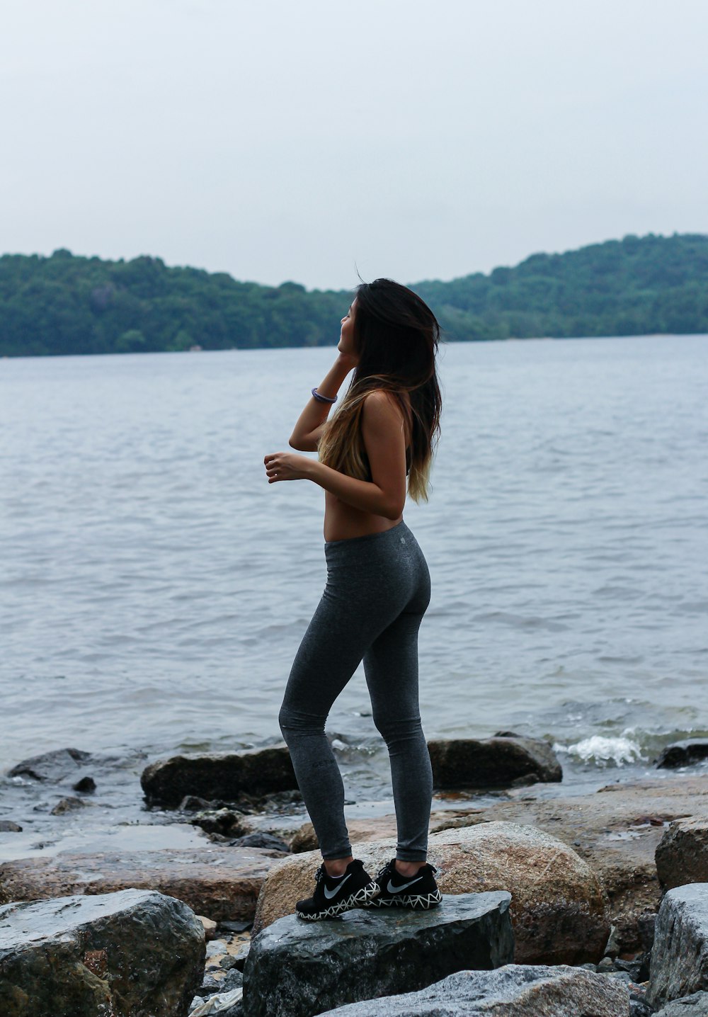 woman in gray leggings standing on rock near body of water during daytime