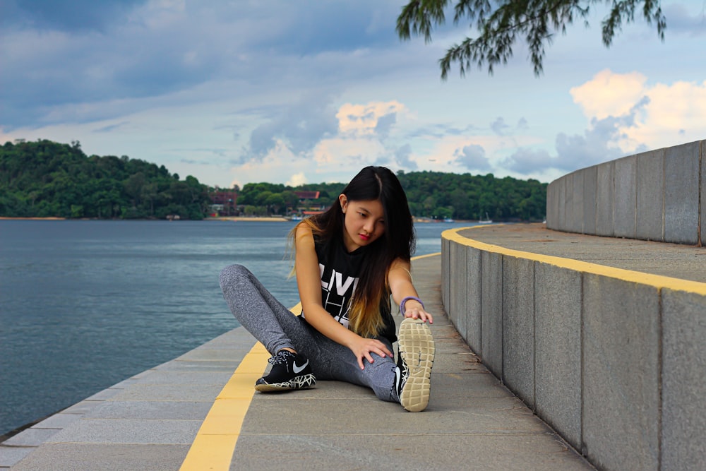 woman in black tank top and gray pants sitting on concrete dock during daytime