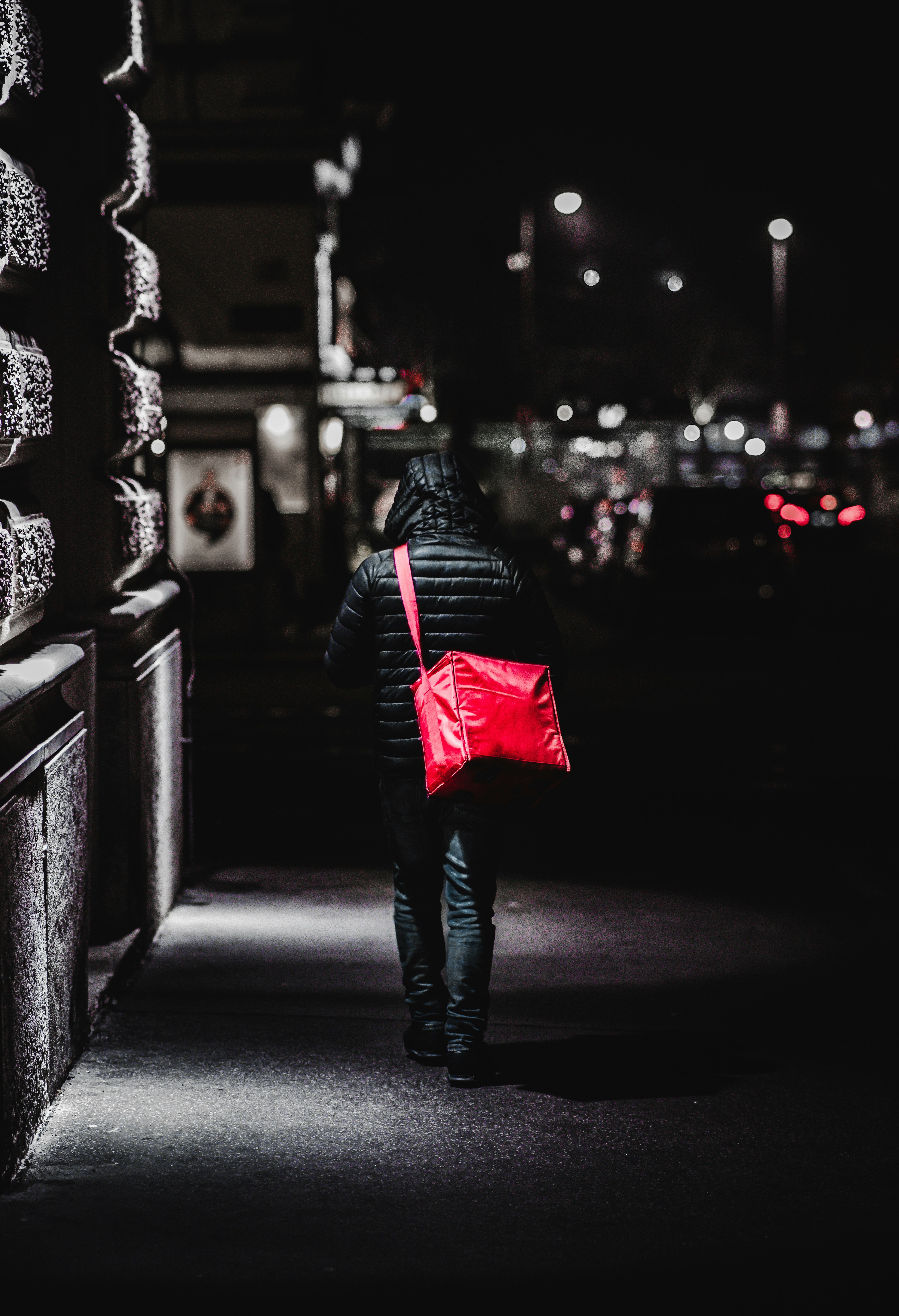 woman in black jacket and blue denim jeans walking on sidewalk during night time