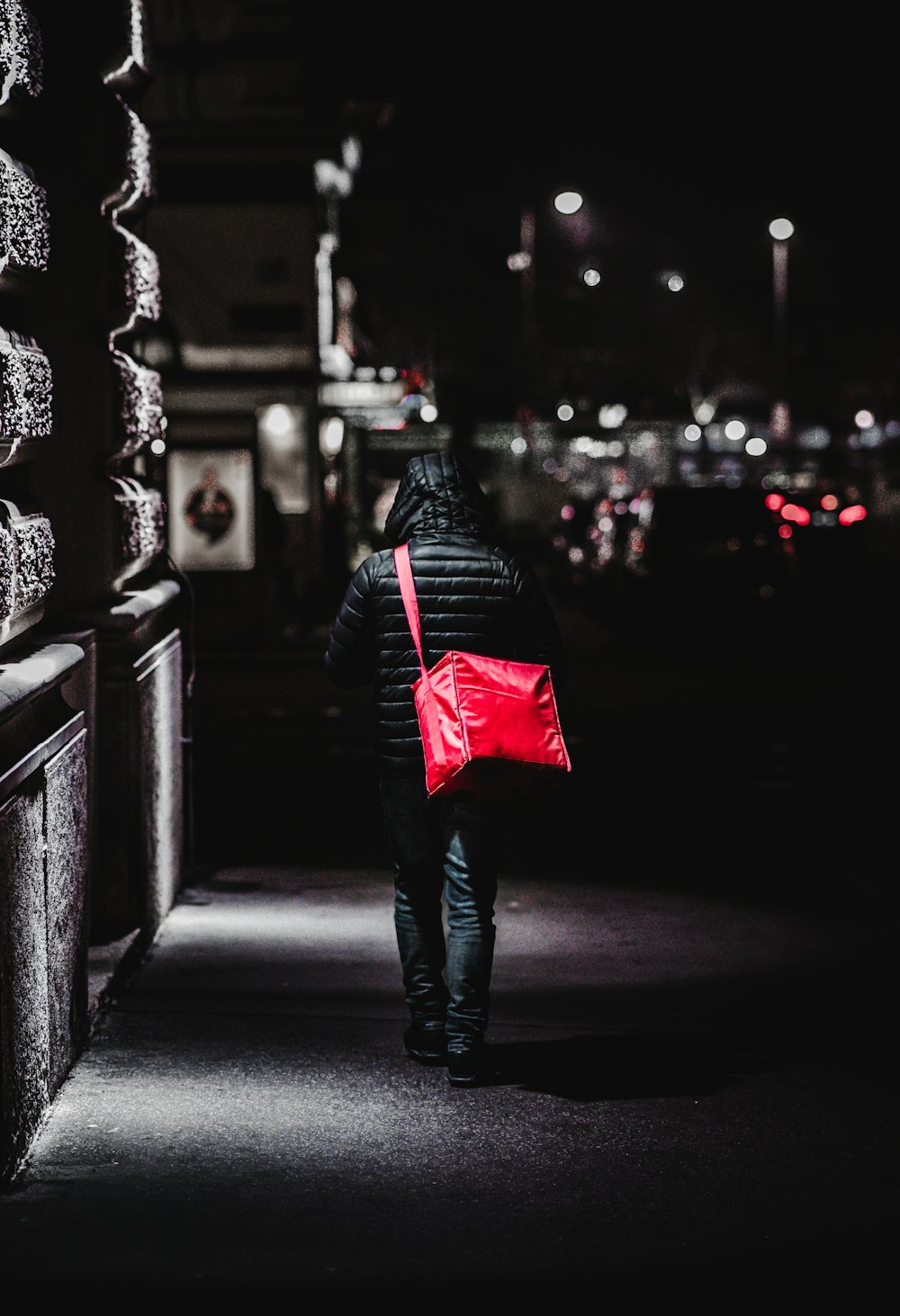 woman in black jacket and blue denim jeans walking on sidewalk during night time