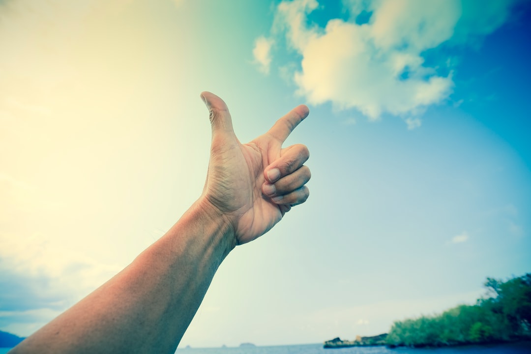 person raising right hand under blue sky during daytime