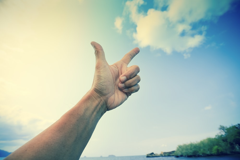 person raising right hand under blue sky during daytime