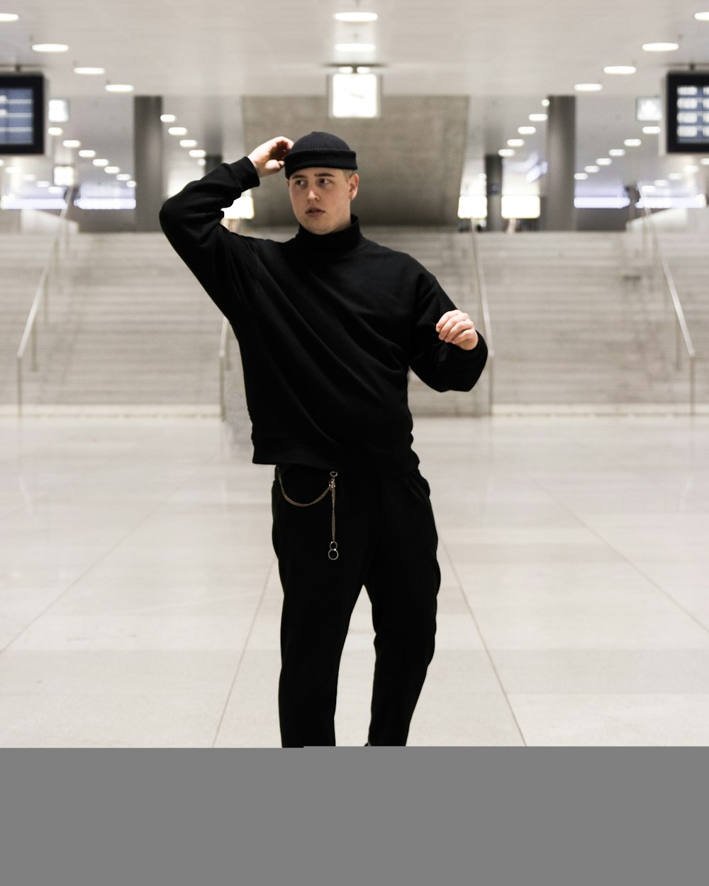 man in black sweater and black pants standing on white floor tiles