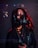 A person wearing a dark hooded cloak and a futuristic, black respirator mask with visible digital text and graphics superimposed around them. Red lighting highlights the edges and creates a dramatic contrast against the dark background.