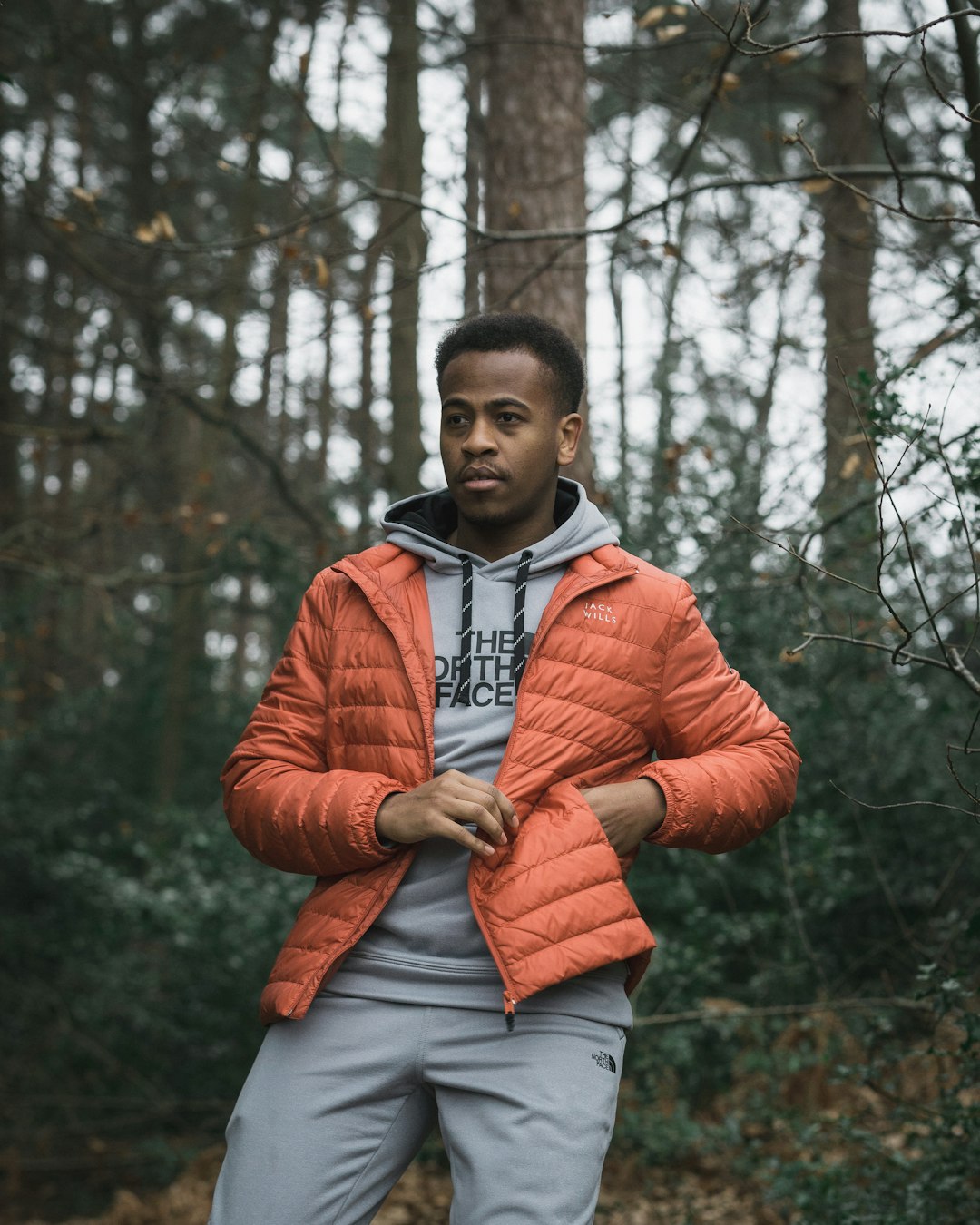 man in red zip up jacket standing near trees during daytime