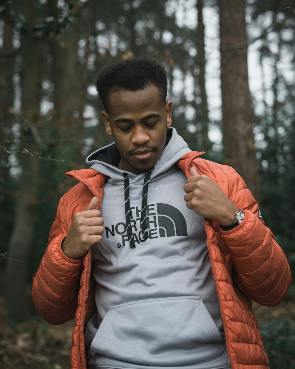 man in orange jacket standing near trees during daytime