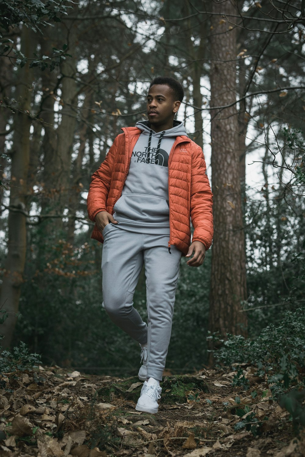 uomo in giacca arancione con zip in piedi vicino agli alberi durante il giorno