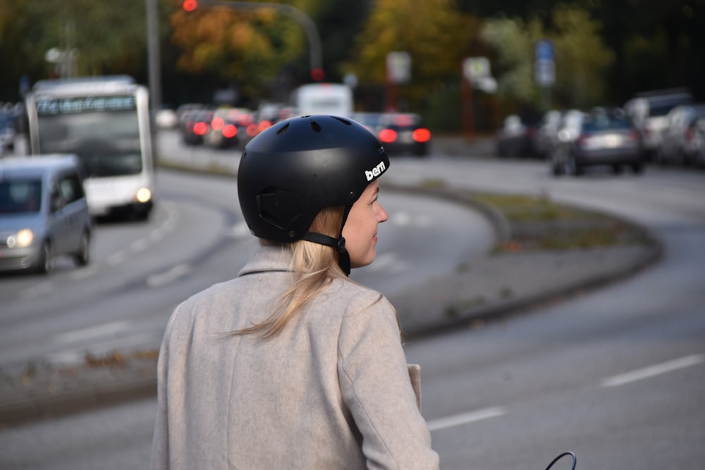 Frau im grauen Mantel mit schwarzem Helm steht tagsüber auf der Straße