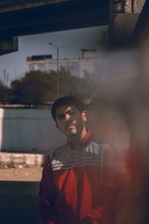A casual urban scene featuring a young person wearing a bold red and blue retro-style sports jacket, with the city skyline softly blurred in the background.