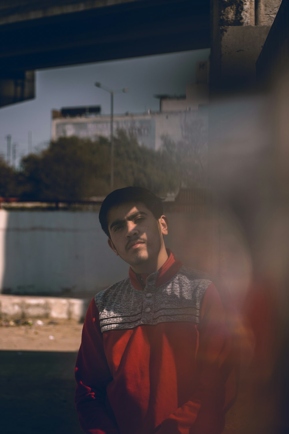 a man standing in front of a bridge wearing a red jacket