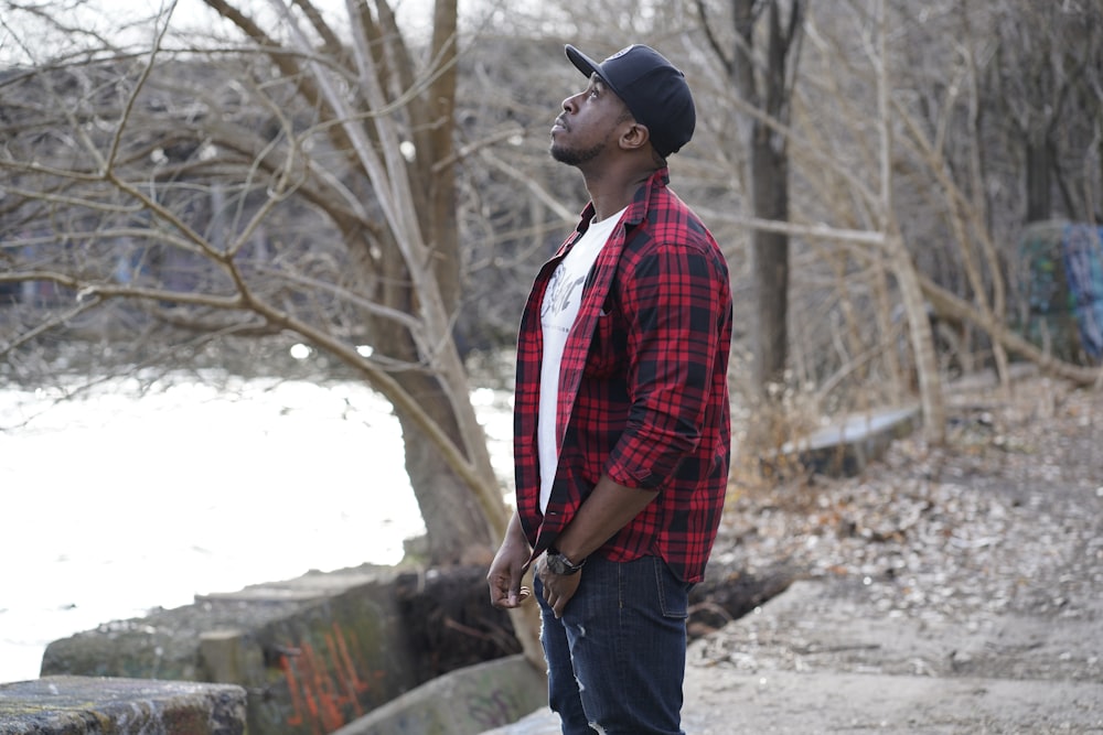 man in red and white plaid dress shirt and blue denim jeans standing near brown tree