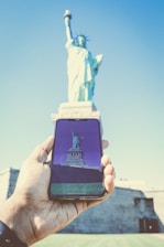 A person holding a smartphone with Canadian landmarks in the background.