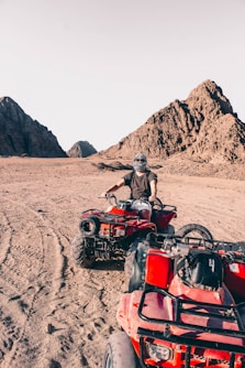 man riding red atv on brown sand during daytime
