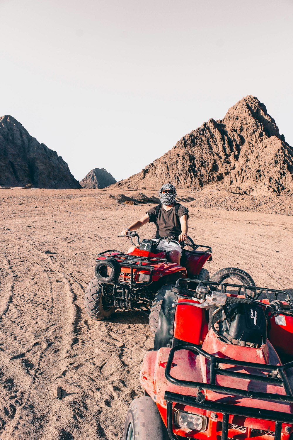 man riding red atv on brown sand during daytime