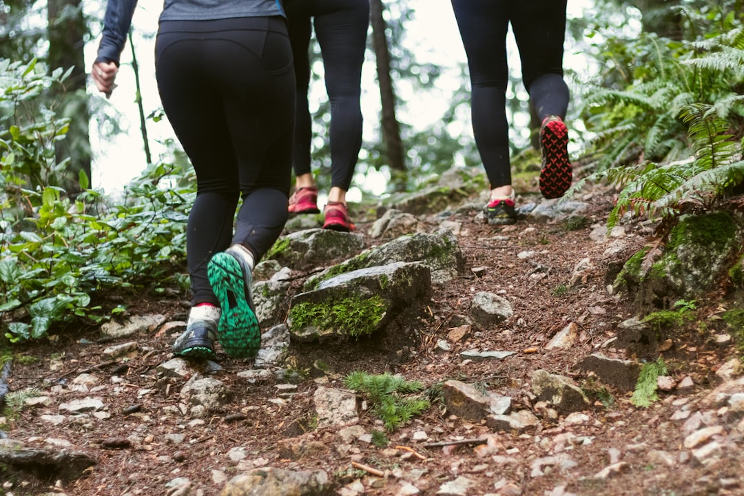 person in black leggings and green sneakers standing on brown rock, group of athletic women in running shoes climbing a 