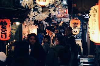 A bustling street in Kyoto lined with wooden shops and red paper lanterns glowing at dusk.